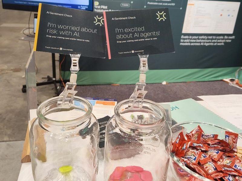 Two glass jars on the counter of the Avesta Labs stand holding voting tokens, the card clipped above one reading I am worried about risk with AI and the card above the other reading I am excited about AI agents, with a bowl of wrapped sweets alongside